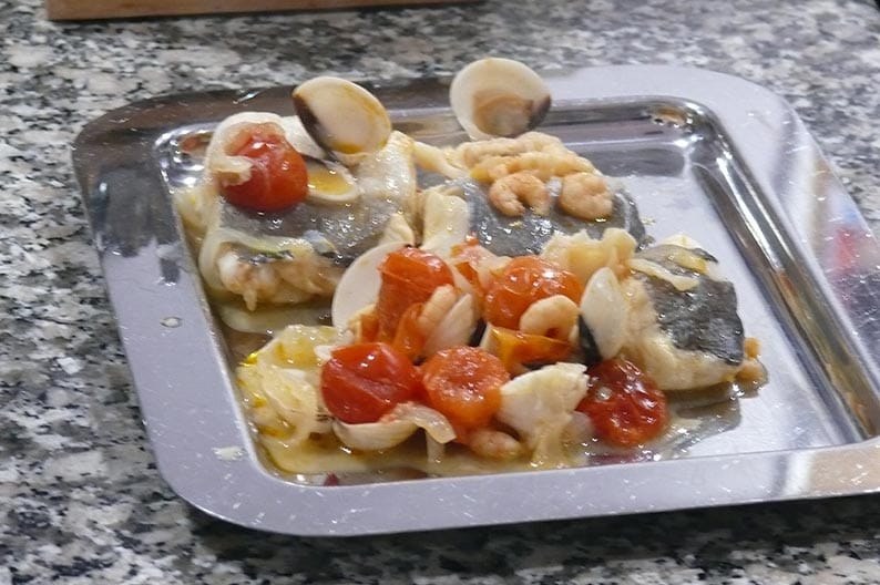 Bandeja metálica con pescado, almejas, gambas y tomates cherry ya cocinados