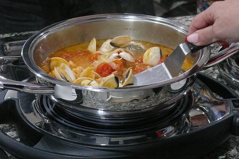 Primer plano de una sartén con almejas y tomates cherry y una espátula metálica